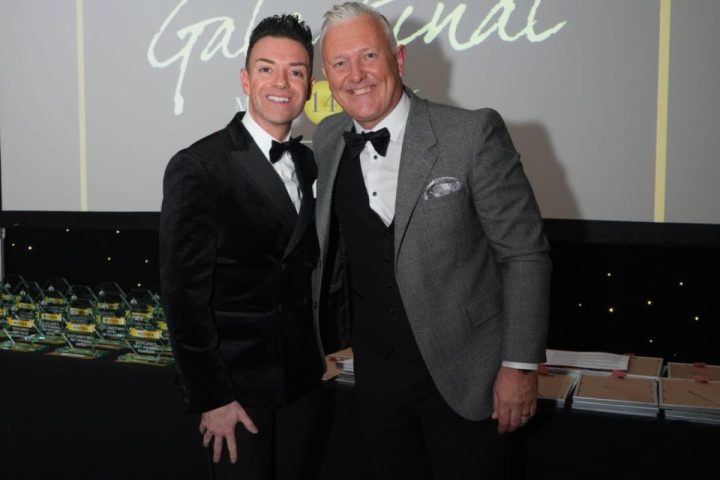 Two hosts in black tie on stage at the Spice Awards Gala Final, with the winners' trophies laid out behind them